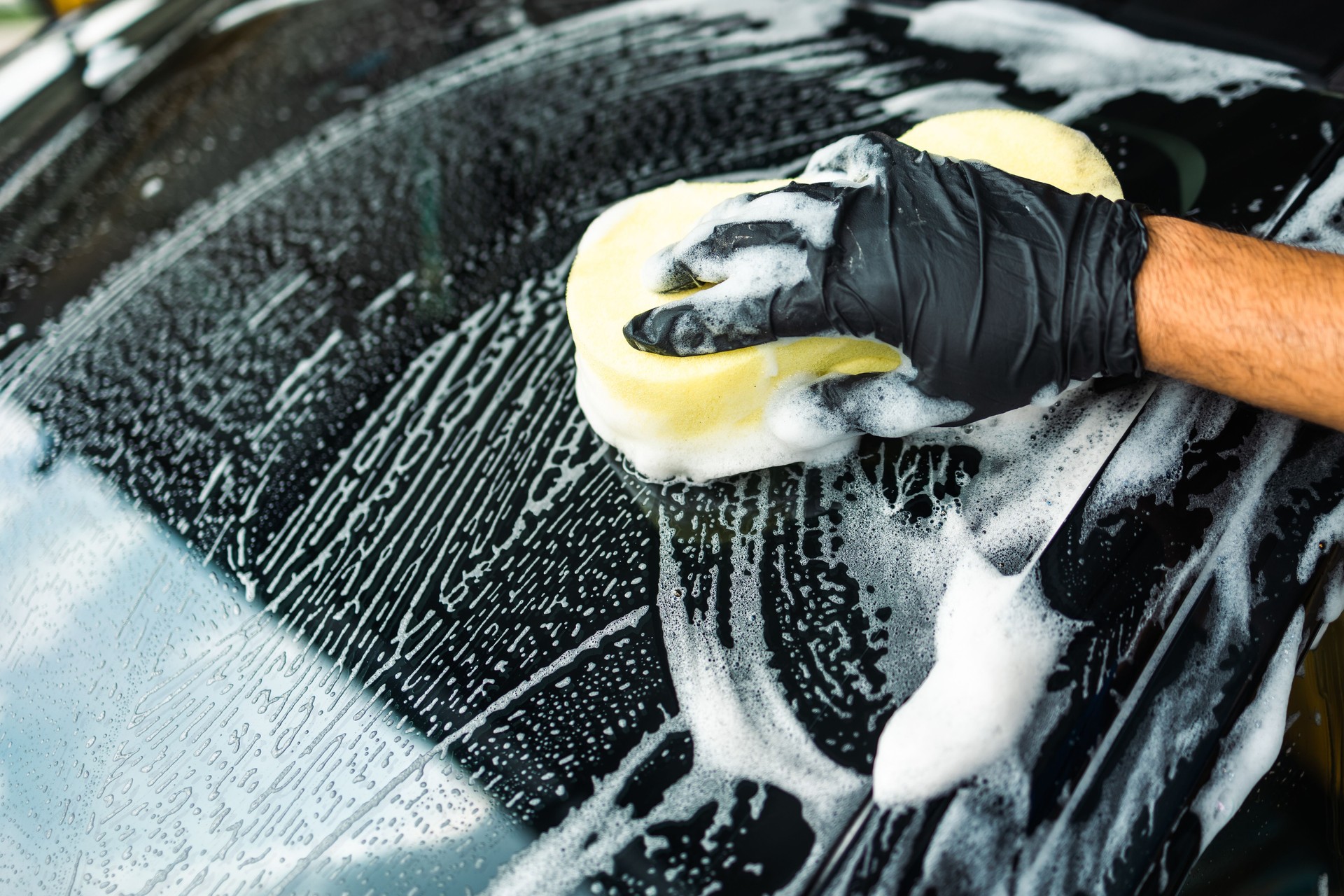 Mann Arbeiter Waschen Autoservice mit Schaum und Schwamm. Wasch-Reinigungs-Wischstation. Mitarbeiter reinigen ein Fahrzeug professionell.