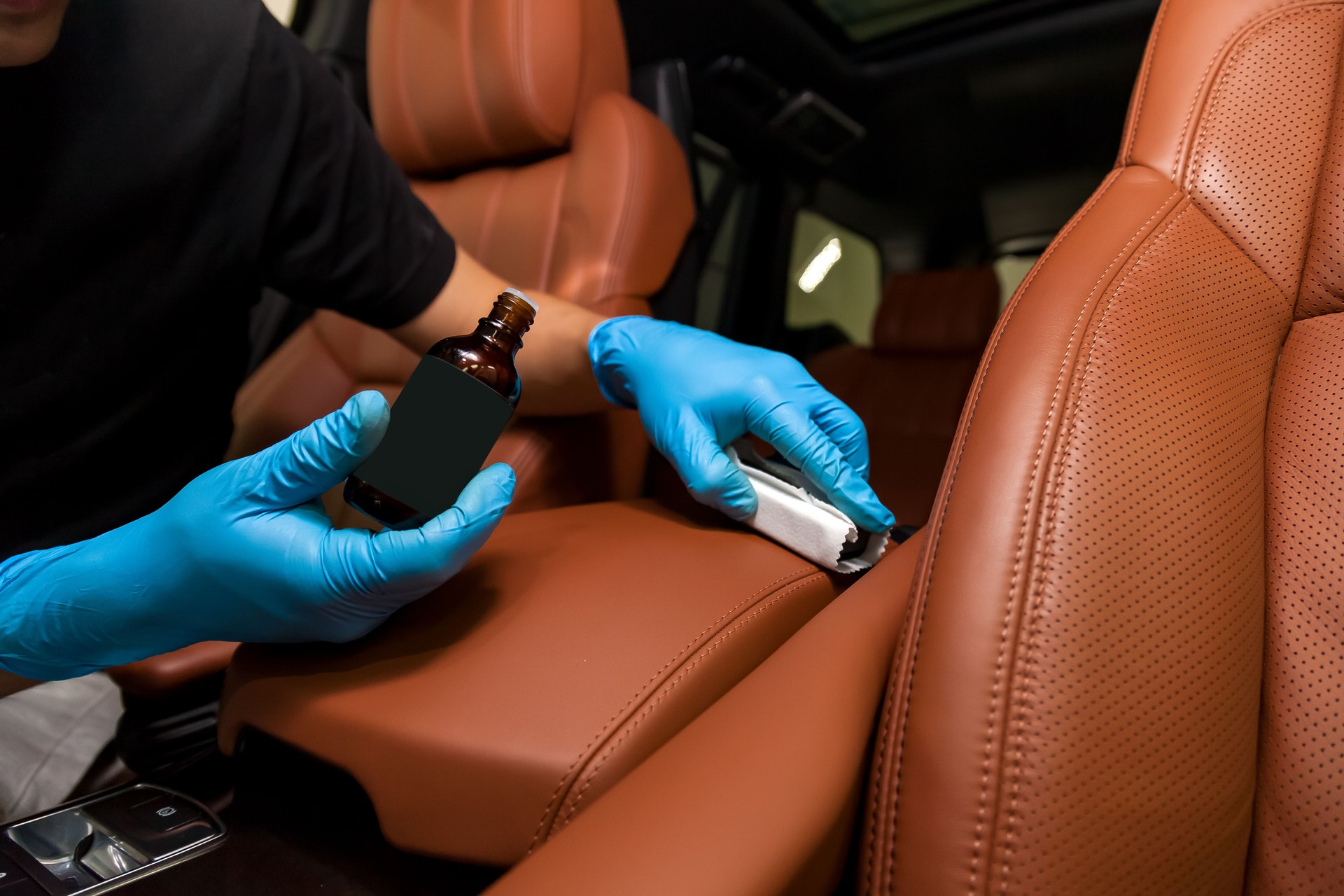 Nano-Keramik-Beschichtung auf Leder des Autositzes braune Polsterung von einem Arbeiter in blauen Handschuhen mit Einem Schwamm und Flasche